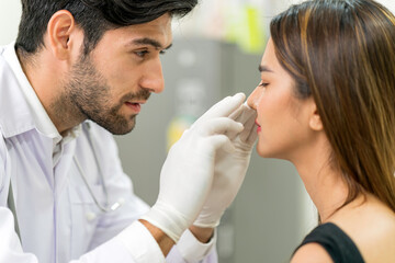 Male surgeon examining young asian female's face in modern clinic.