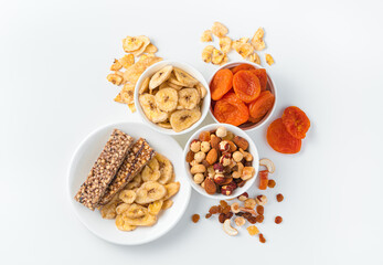Granola bar, nuts and dried fruits on a light background with white plates. Top view, horizontal.
