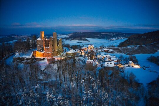 Luftaufnahme von Burg Hanstein und dem Dorf Rimbach im Winter am Abend mit Beleuchtung