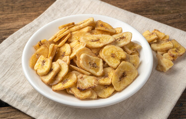 Banana chips in a white plate on a linen napkin. Side view.