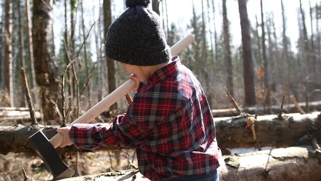 Portrait of a child lumberjack. Little girl with a big ax in a red plaid shirt in the forest. Lumberjack's daughter