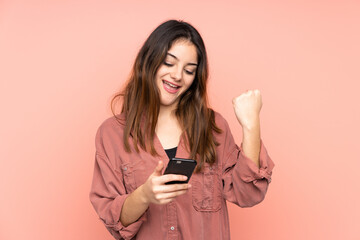 Young caucasian woman isolated on pink background with phone in victory position