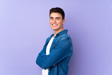 Teenager caucasian  handsome man isolated on purple background with arms crossed and looking forward