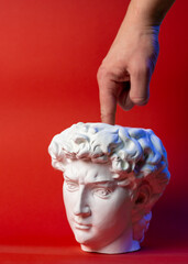 Plaster pot in the form of David's head and male hand on a red background.