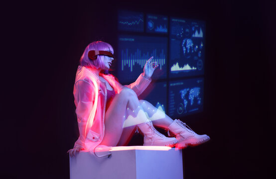 Beautiful woman with purple hair in futuristic costume on dark background. Girl in glasses of virtual reality. Augmented reality game, future technology, AI concept. Holographic interface.