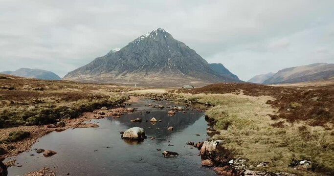 4k aerial footage moving backwards to show Buachaille Etive Mor mountain reflected in water of River Coe. Scottish Highlands, UK.