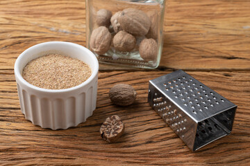 Nutmegs with grater over wodden table. Nutmeg powder in a bowl