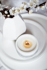 Blooming apricot tree branches and burning candle on round tray in bedroom interior, white spring home decoration