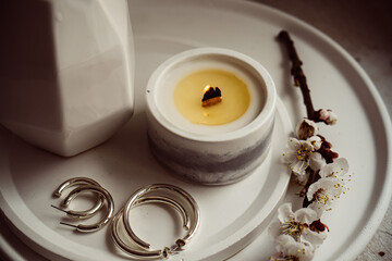 Blooming apricot tree branches in vase and burning candle on round tray in home interior