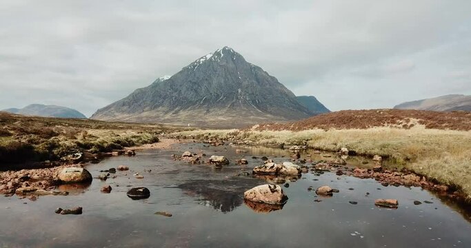 Buachaille Etive Mor and Rannoch Moor in Scottish Highlands. Aerial footage over River Coe with mountain reflected in water. Lifting upwards to show panoramic view of landscape.