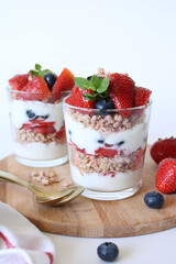 Diet breakfast: homemade yogurt with crispy oatmeal, strawberries, blueberries on a white plate.