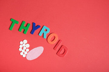 silhouette of the thyroid gland from pills and pink felt and the inscription thyroid on a red...