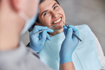 Cheerful positive dentist and client in dentistry. Female patient at dental procedure, doctor using...