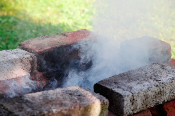 Holidays outdoors. Self-made grill made of bricks put in the garden with the smoke coming out of it. Close-up.