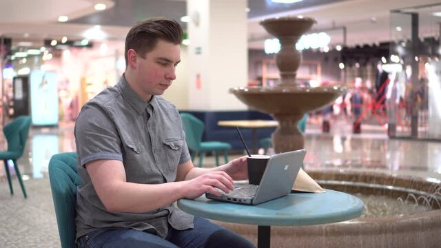 Young man in a cafe with a laptop on the background of a fountain. Decoration in the cafe.