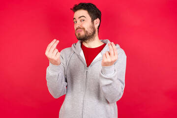 Young caucasian man wearing tracksuit over red background doing money gesture with hands, asking...