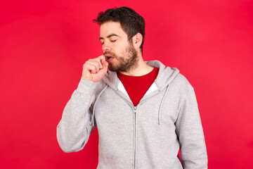 Young caucasian man wearing tracksuit over red background feeling unwell and coughing as symptom...