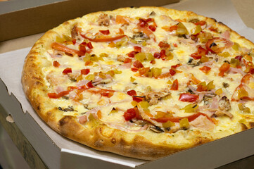 Pizza with a fried appetizing crust with pineapple, tomato, pepper, ham and plenty of cheese in a box for delivery to the customer