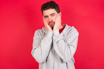 Young caucasian man wearing tracksuit over red background Tired hands covering face, depression and sadness, upset and irritated for problem