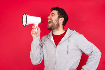 Funny Young caucasian man wearing tracksuit over red background People sincere emotions lifestyle concept. Mock up copy space. Screaming in megaphone.