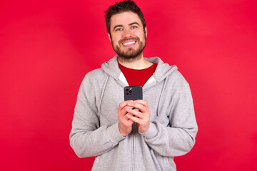 Young caucasian man wearing tracksuit over red background Mock up copy space. Using mobile phone, typing sms message