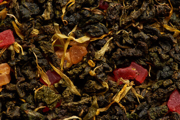 Tea leaves texture with flower petals and fruit pieces as a background.