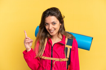 Young mountaineer man with a big backpack isolated on yellow background showing and lifting a finger in sign of the best