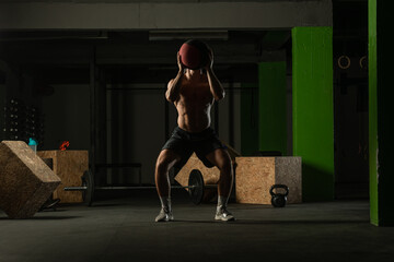 Fit man throwing medicine ball doing ball slam against gym floor or shoulder press exercise..
