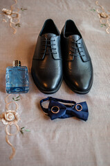 Accessories for the groom. Black leather shoes, gold wedding rings, blue bow tie, perfume