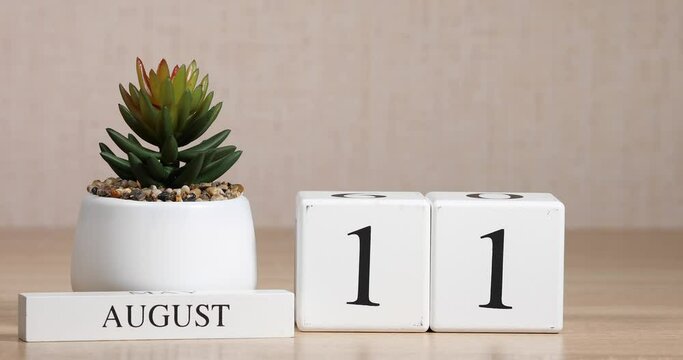 Wooden calendar with an important event for August 11, a woman's hand sets the date on the calendar. Summer season.
