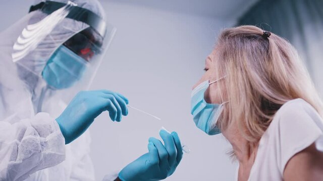 Black doctor in full uniform performing nasal swab covid tes on an elderly woman. High quality 4k footage