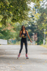 Hot athletic woman in sportswear rollerblading at the park in sunny weather..