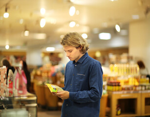 Young man shopping in supermarket, reading product information