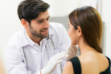 Male surgeon examining young asian female's face in modern clinic.