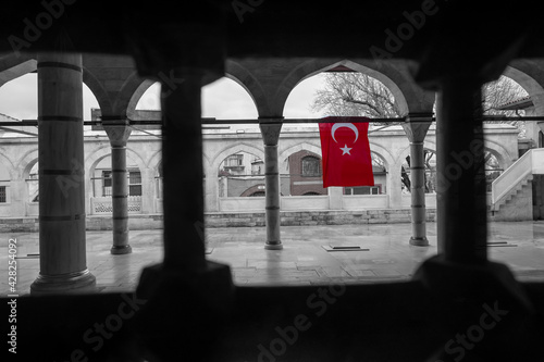 framing of highlighted Turkish flag hanging on iron fence in mosque garden from behind a window with low saturation environment