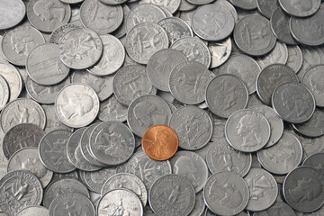 Single USD copper penny stands out alone in a pile of silver quarters