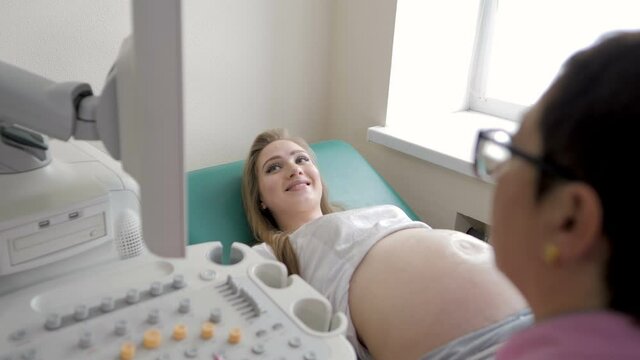 A professional female doctor with glasses makes a 3D ultrasound of the abdominal cavity of a pregnant woman in the clinic. The doctor uses ultrasound equipment when examining a pregnant woman.