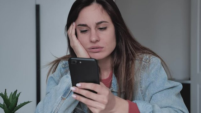 Attractive millenial woman serfing news in smartphone. Boredom in the office. Unloved job.