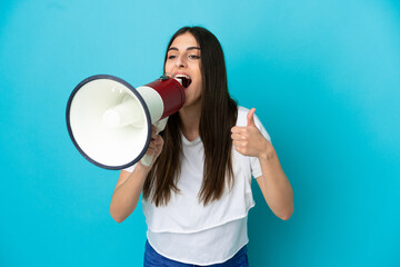 Young caucasian woman isolated on blue background shouting through a megaphone to announce...