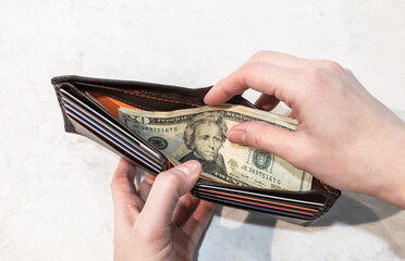 Person look and hold 20 dollar banknote inside opened brown wallet on white marble background, cash left of daily life after shopping.