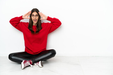 Young woman sitting on the floor isolated on white background with surprise expression