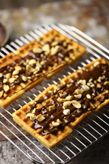 French waffles on a wire rack, drizzled with chocolate and sprinkled with nuts.