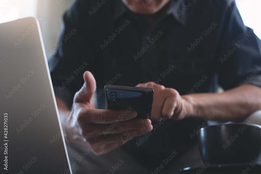 Poster man using mobile phone during working on laptop computer on table, close up