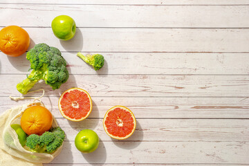 Juicy red oranges grapefruits, green broccoli in ecological handbag mesh on a wooden table in bright sunlight. Diet fresh dessert for vegan food. The idea of avoiding plastic bags