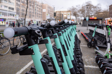 Close up and selected focus view at handle, row of E-scooters with Eco friendly mobility concept of sharing Electric Scooter, park on street in front of train station in Düsseldorf, Germany.