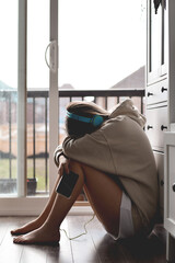 Young teenage girl in headphones sitting on a kitchen floor sad or upset with her head down on her...