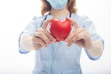 Doctor woman stands in a protective mask with a stethoscope and holds a heart in her hands isolated on white background