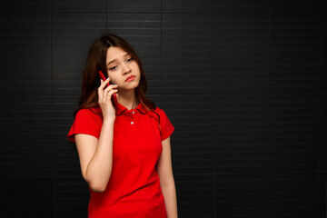 A beautiful young girl in a red T-shirt with a red phone in her hands. Technology and mobile...