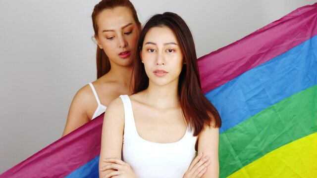 pretty lesbians couple asian  woman  celebrate parade show tolerance same sex marriages hugging hold gay rainbow flag wear casual t-shirts isolated white color background.