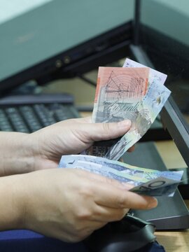 hands of a woman holding Australian money on a computer keyboard